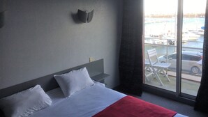 Ein Hotelzimmer mit einem Bett, einem Fenster mit Blick auf Boote und Autos sowie einer Wandleuchte.