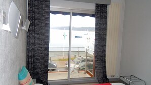 Ein Hotelzimmer mit Bett, einem Fenster mit Vorhängen, Blick auf Boote auf dem Wasser und einem Balkon mit Stühlen.