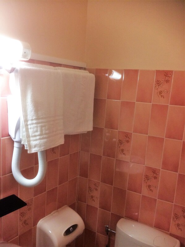 Ein Badezimmer mit einer weißen Toilette, einem Handtuchhalter mit zwei weißen Handtüchern und pink gefliesten Wänden mit floralen Mustern.