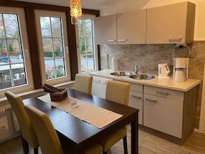 A modern kitchen with a dark wooden table, two chairs, a built-in sink, and a coffee maker. - Apartment in the former farmhouse, with beams and lattice windows (Lübeck)