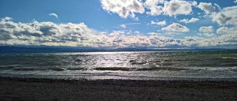 A beach with a pebbly shore and a view of the ocean under a partly cloudy sky.