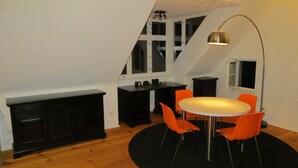 Une cuisine compacte avec un coin repas, comprenant une table ronde entourée de quatre chaises orange, un meuble noir et un grand lampadaire.