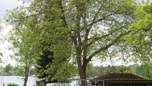 Une zone au bord du lac, bordée d’arbres, avec un espace de stationnement clôturé où se trouvent un fourgon blanc et un bateau bleu.