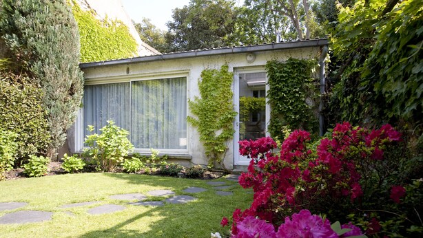 Ein Garten mit einem Haus, einem Kiesweg und blühenden Pflanzen.