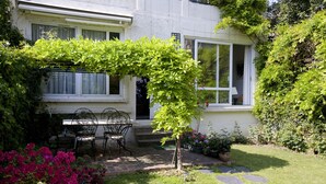 Ein Haus mit Terrasse, Tisch, Stühlen und einem kleinen Baum.