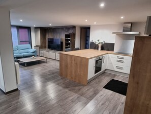 Et moderne køkken med ø, integrerede hårde hvidevarer og en spiseplads med sofa og sofabord.
