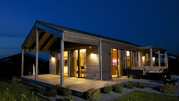 Ein modernes Haus mit überdachter Veranda, großen Fenstern und einem gut beleuchteten Innenraum.