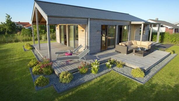Une maison moderne dotée d’un patio couvert, de mobilier d’extérieur et d’un jardin bien entretenu.