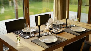 Une table à manger dressée pour quatre personnes, avec des bougies, des verres à vin et des assiettes, donnant sur un jardin.