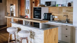 Una cocina moderna con una isla de madera, taburetes, microondas, cafetera y un lavamanos.