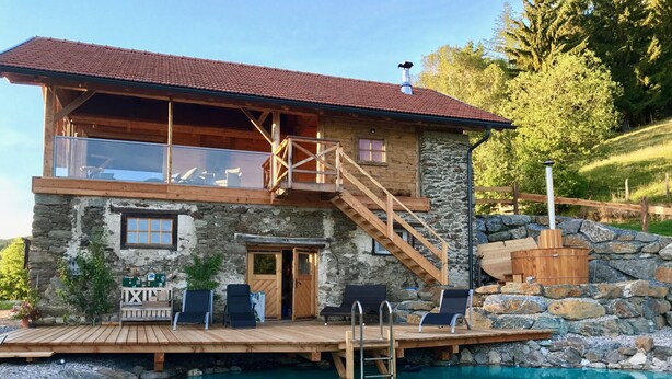 Un edificio de piedra de dos plantas con un deck de madera y una piscina.