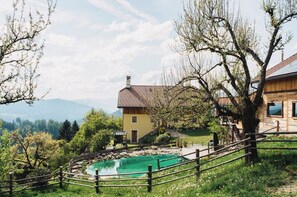 A yellow building with a tiled roof, a wooden fence, and a swimming pool surrounded by greenery and trees.