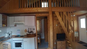 A rustic cabin interior with a kitchen area, wooden staircase, and a dining area.
