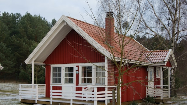 A red wooden house with a white porch and a chimney.