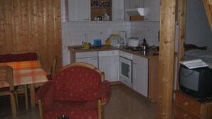 A compact kitchen with a dining area, wooden walls, and a television.