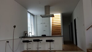 Una cocina moderna con una isla central, taburetes de bar, una cafetera y un ventanal con persianas.