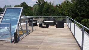 Terraza de madera con mobiliario exterior y cerramiento de vidrio.