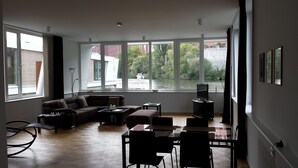 Una sala moderna con sofá, una mesa de centro y un mueble para la televisión. Ventanas amplias ofrecen vistas a un río y edificios.