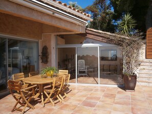 An outdoor patio with a wooden table and chairs, a potted plant, and a sliding glass door leading to an interior space. - Beautiful villa at Mt des Oiseaux with 180° sea view and heated whirlpool pool (Var)