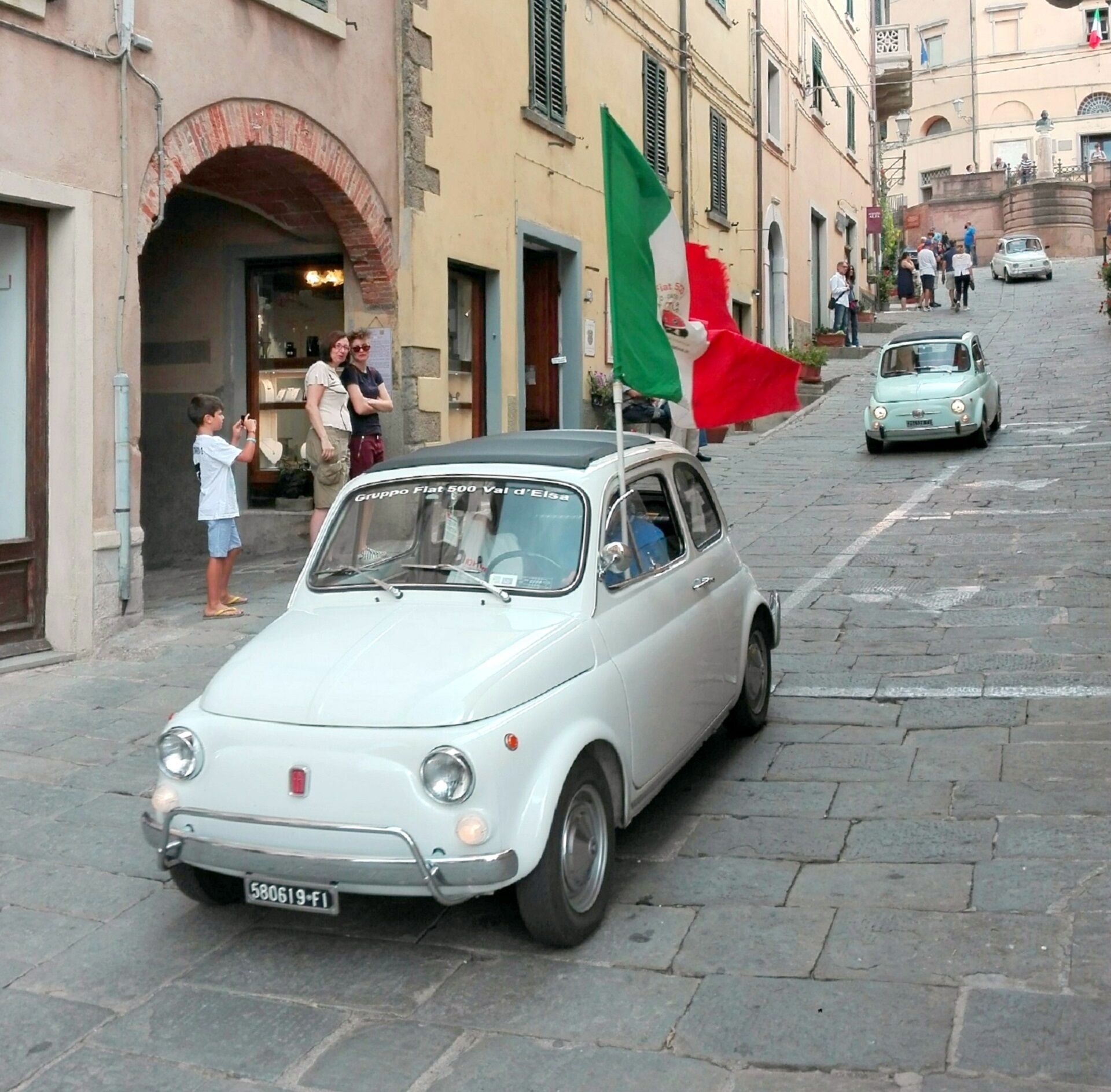 Vanha Fiat 500 -malli ajamassa mukulakivikatua, taustalla historiallisia rakennuksia.