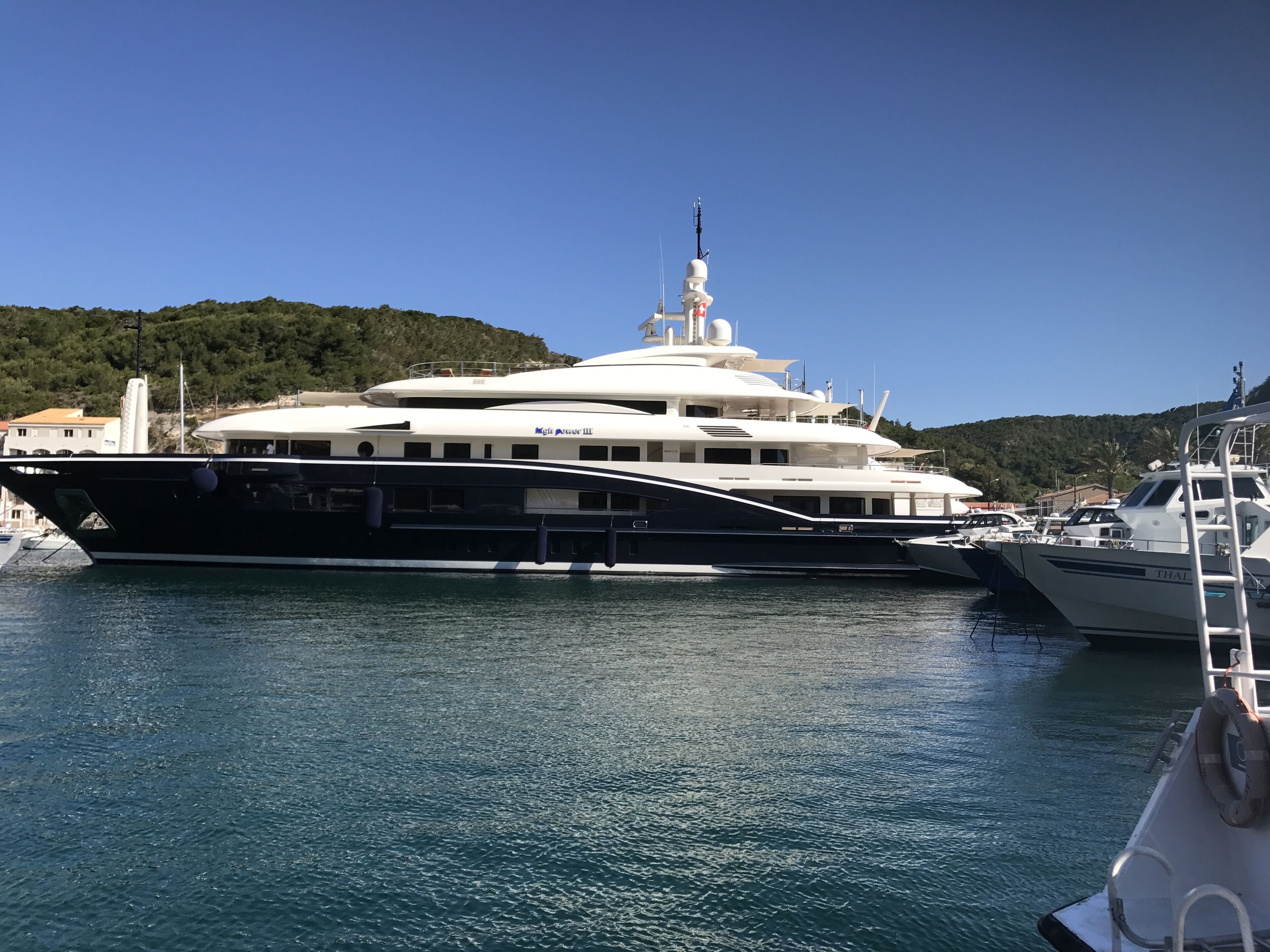 A large yacht docked at a marina with a mountainous backdrop.