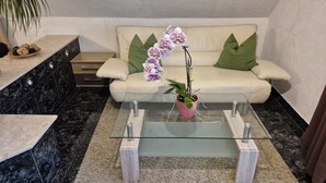 Un salon moderne avec une table basse en verre, un canapé beige agrémenté de coussins verts et une plante orchidée en pot.