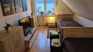 Une chambre à coucher accueillante et compacte, avec un lit en bois, un petit bureau doté d’une lampe, une télévision et une fenêtre ornée d’orchidées en pot.