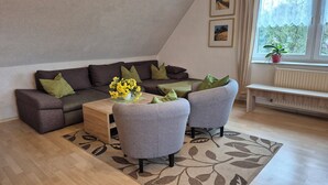 Un salon moderne avec un canapé marron foncé, deux fauteuils gris, une table basse en bois et un tapis à motifs.