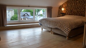 A bedroom with a large window, a bed with a patterned bedspread, and a stone wall. - Gîte Histoire d'Ardenne with sauna in the historic center of La Roche (La Roche-en-Ardenne)