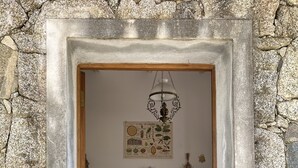 A stone-framed doorway leading to a dining area with a table set for two, a wooden cabinet with dishes, and a wall-mounted light fixture. - Caseddu charming, small typical Corsican sheep (Sartène)