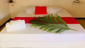 Un llit ben fet amb un coixí vermell, roba de llit blanca i una fulla tropical al damunt.
