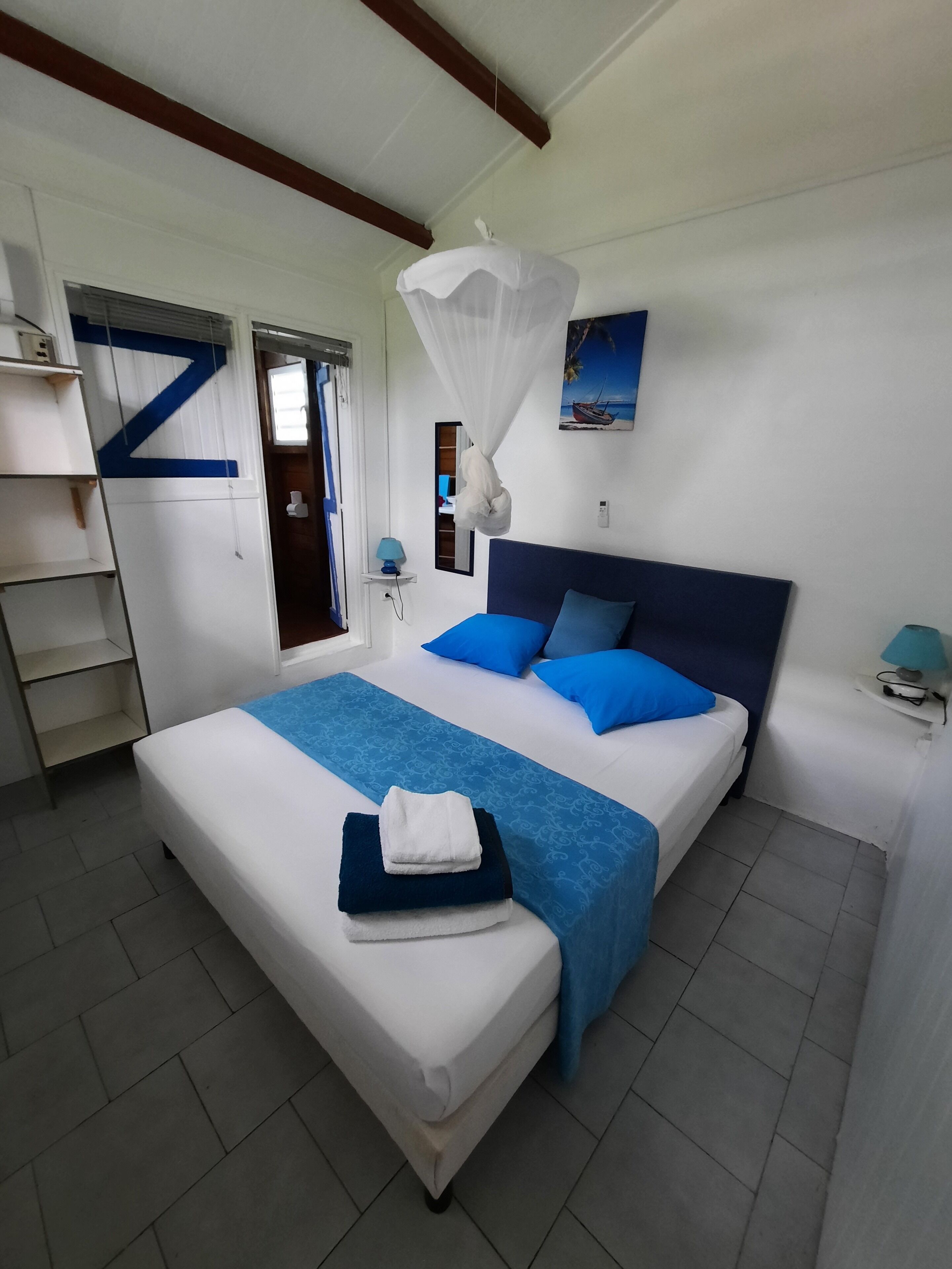 A bedroom with a bed, a nightstand, a shelf, and a window with curtains.