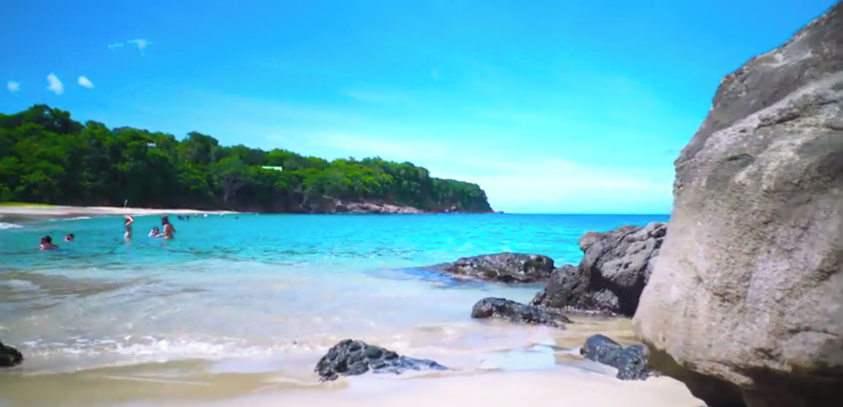 Une plage avec une eau claire, des rochers et une zone boisée en arrière-plan.
