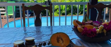 A breakfast setting with a view of the ocean, featuring a plate of eggs, toast, a bowl of fruit, and a glass of juice.