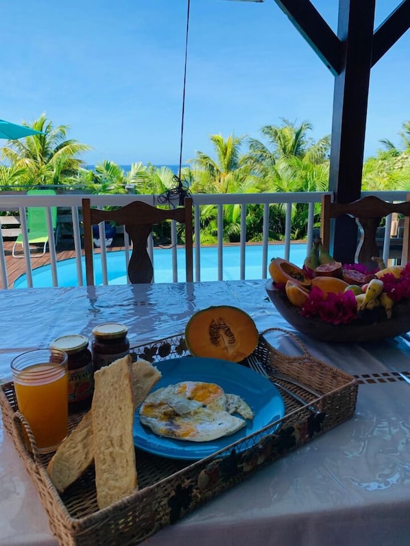 Un desayuno con vista al océano, que incluye un plato de huevos, tostadas, un bol de fruta y un vaso de jugo.