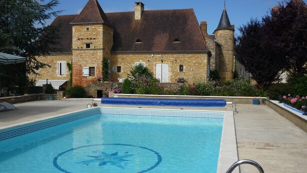 Una piscina con un diseño decorativo de estrellas, rodeada por un edificio de piedra con una torre y un patio cubierto.