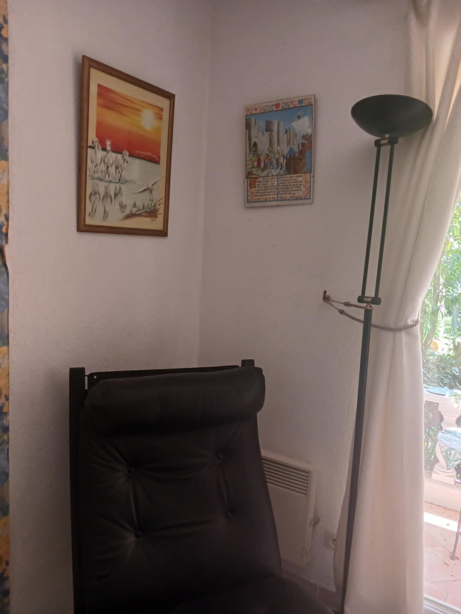 Une pièce avec une chaise noire, un lampadaire et deux tableaux encadrés accrochés au mur.