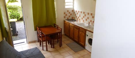 Una cocina compacta con una mesa y sillas, lavadora y ventana con persianas.