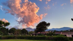 Un paysage comprenant une formation nuageuse importante, des arbres et une chaîne de montagnes en arrière-plan.