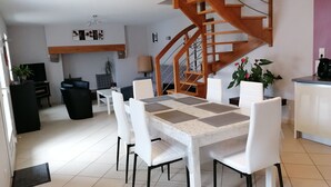 Un comedor con una mesa y sillas blancas, una escalera y una zona de cocina con una cafetera.