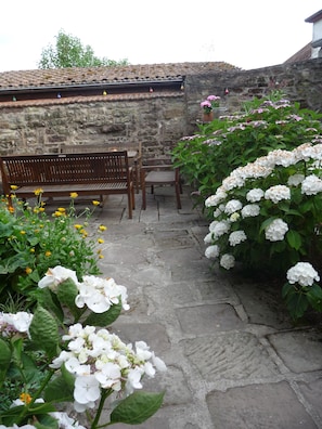 Relax in a serene outdoor seating area surrounded by lush greenery and vibrant flowers.