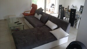 Un salon moderne avec un canapé marron foncé, des coussins blancs, une table basse en verre et un fauteuil rouge.