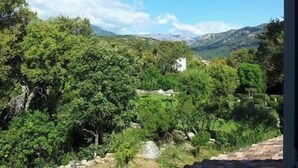 Un paysage montagneux, avec une végétation luxuriante et un bâtiment blanc qui se dessine à l’horizon.