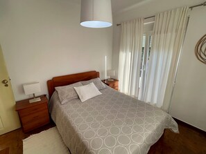 Un dormitorio con cama, mesitas de noche, lámpara y ventana con cortinas.