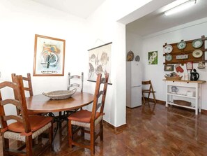 A dining area with a round table, wooden chairs, and a white refrigerator in the background.
