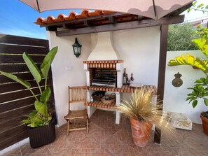 An outdoor patio with a built-in grill, seating, and potted plants. - Matias Terrace House (Lourinhã)