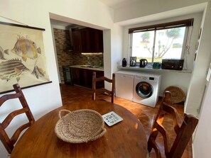 Una cocina compacta con lavadora, una mesa de comedor con sillas y una ventana con vistas a palmeras.