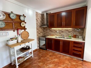 A kitchen with wooden cabinets, a stove, a sink, and a tiled backsplash. - Casa Matias - Charming Portuguese Beach House (Lourinhã)