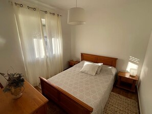 A bedroom with a bed, a bedside table, a lamp, a curtain, and a small plant. - Matias Terrace House (Lourinhã)
