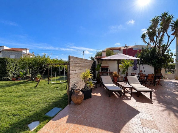 A patio with a swing set, outdoor furniture, and a tiled floor.
